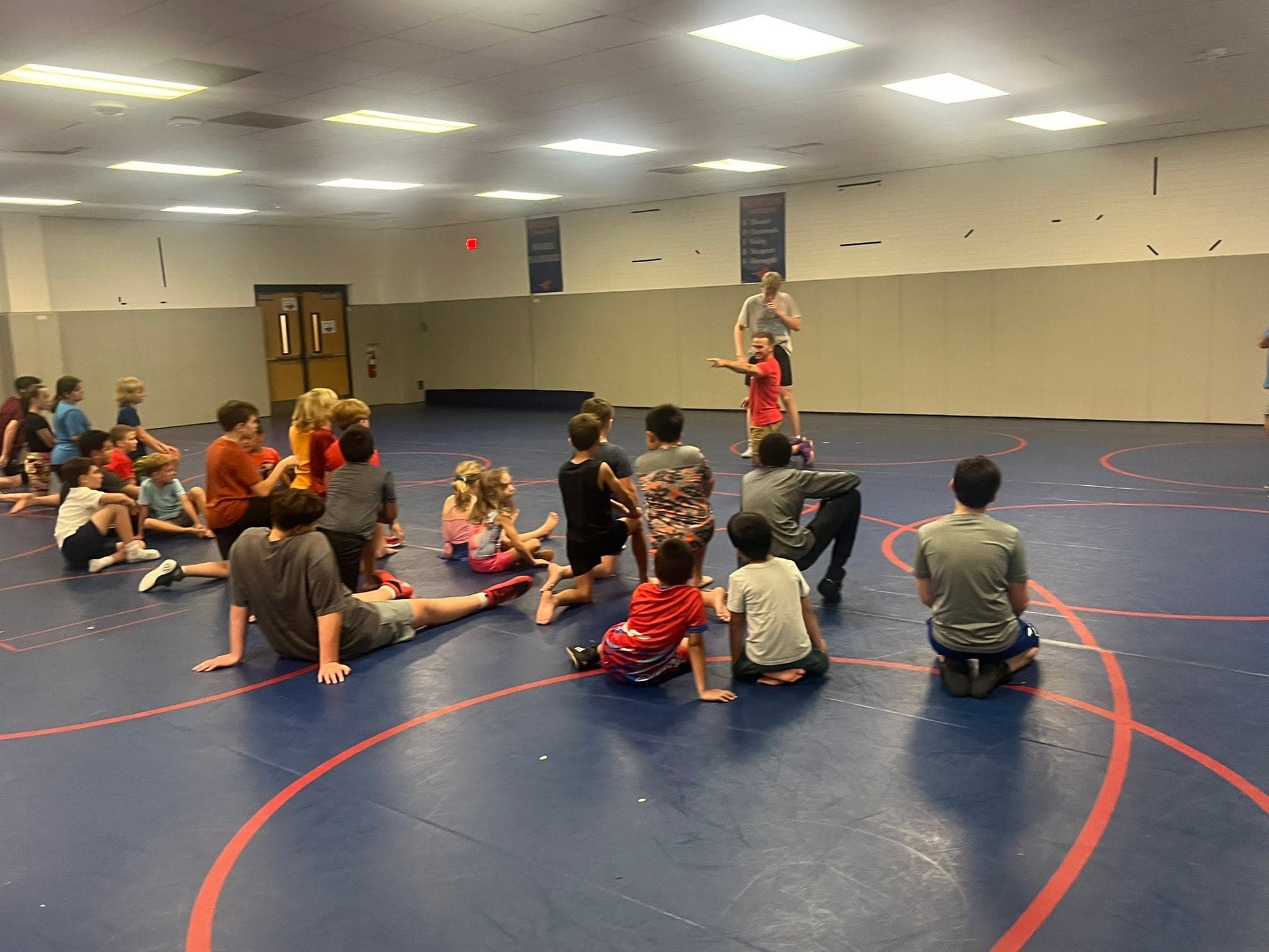 Coach giving instruction to kids seated on the wrestling mat