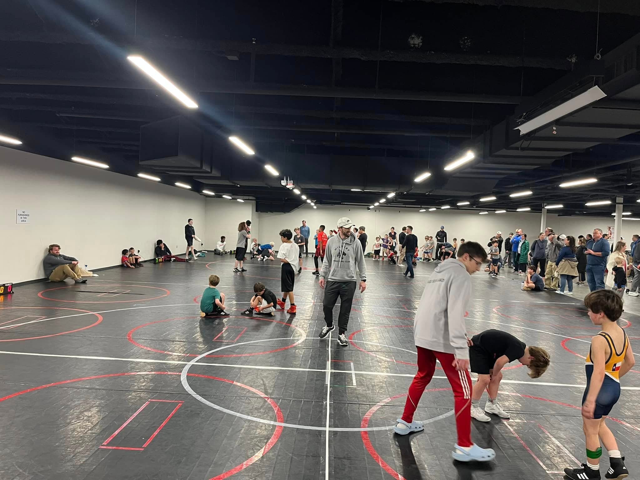 Wrestlers warming up and drilling across an open practice mat