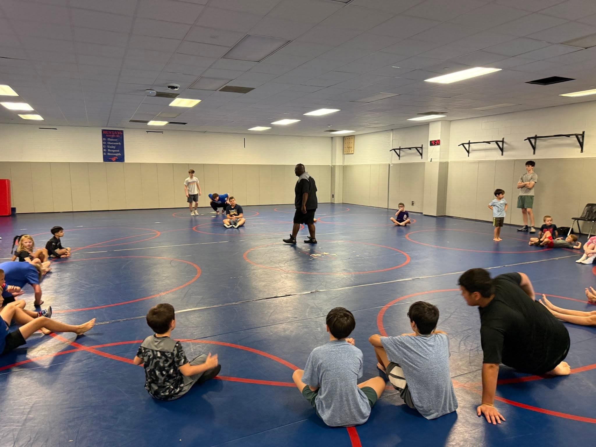 Young wrestlers seated in a circle listening to a coach during practice